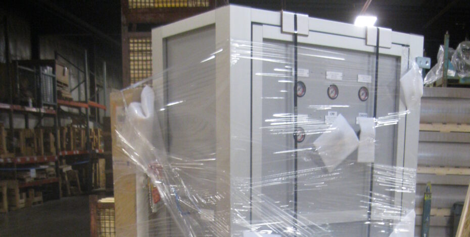 A custom-made machine kit box with plastic wrap around it. The box is tied down to a custom-made pallet with back support using black tie-downs.