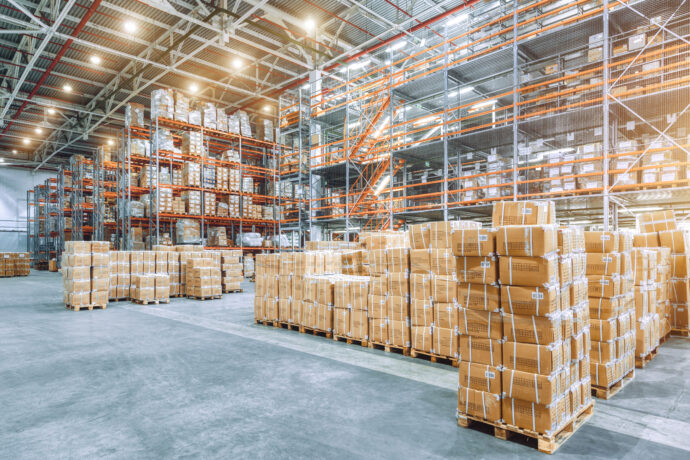Large industrial warehouse with high racks. In the foreground are a lot of cardboard boxes.